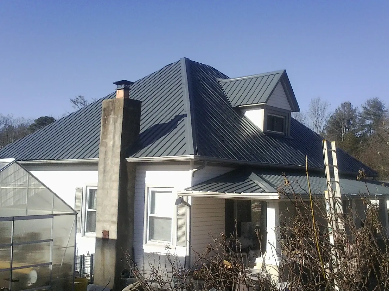 Dark blue standing seam metal roof on a white farmhouse with dormer — Slate & Tile Roof Repair by Roofing Brothers in Sumter