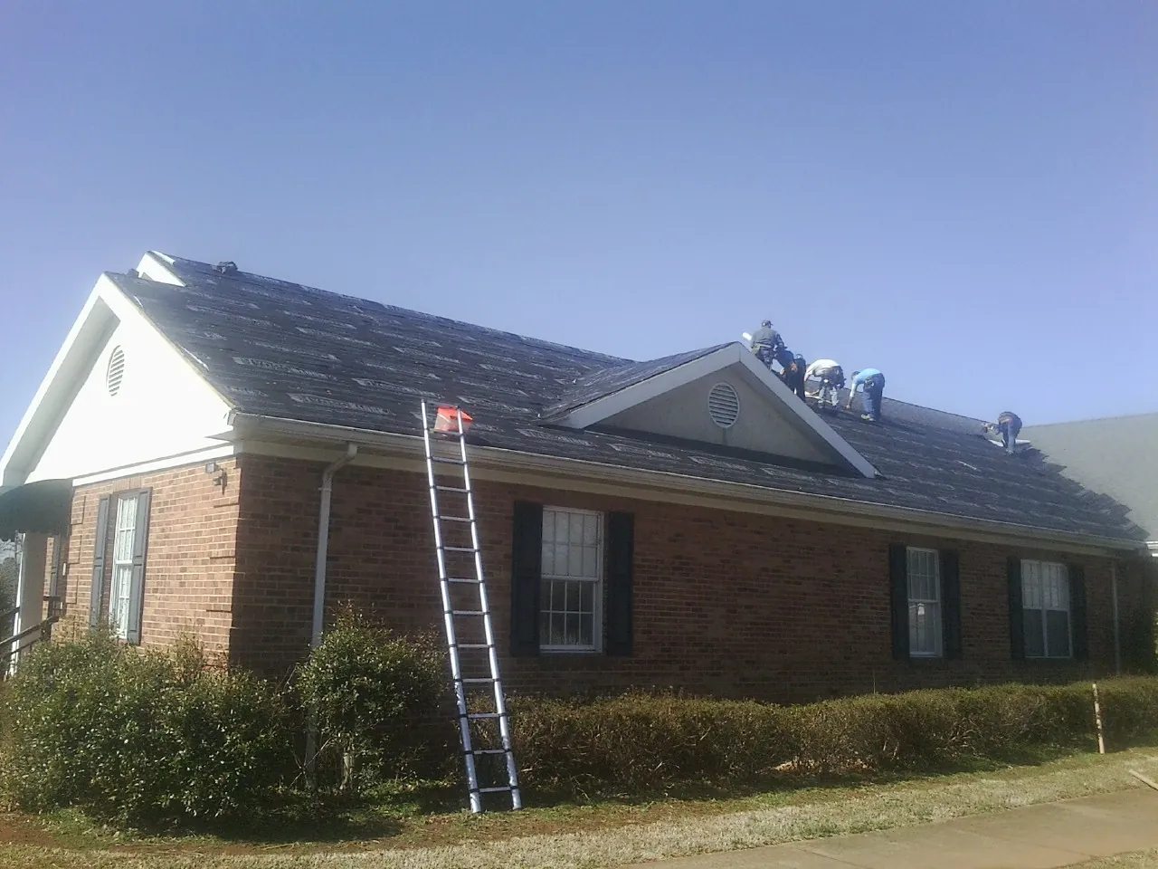 Crew tearing shingles off a brick ranch roof with a ladder set — Metal Roof Repair work by our crew in Sumter