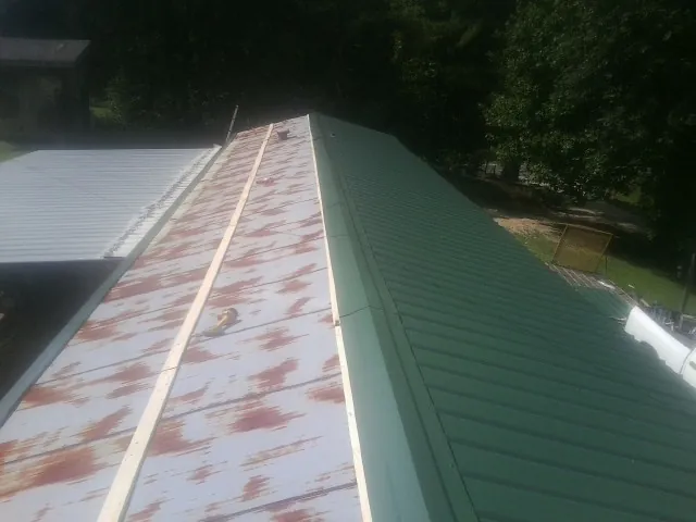 Old rusted panels beside newly installed green metal roofing — Wind Damage Roof Repair by Roofing Brothers in Sumter