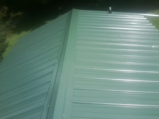 New green metal panels meeting at the ridge of a roof — Flat Roof Repair work by our crew in Sumter