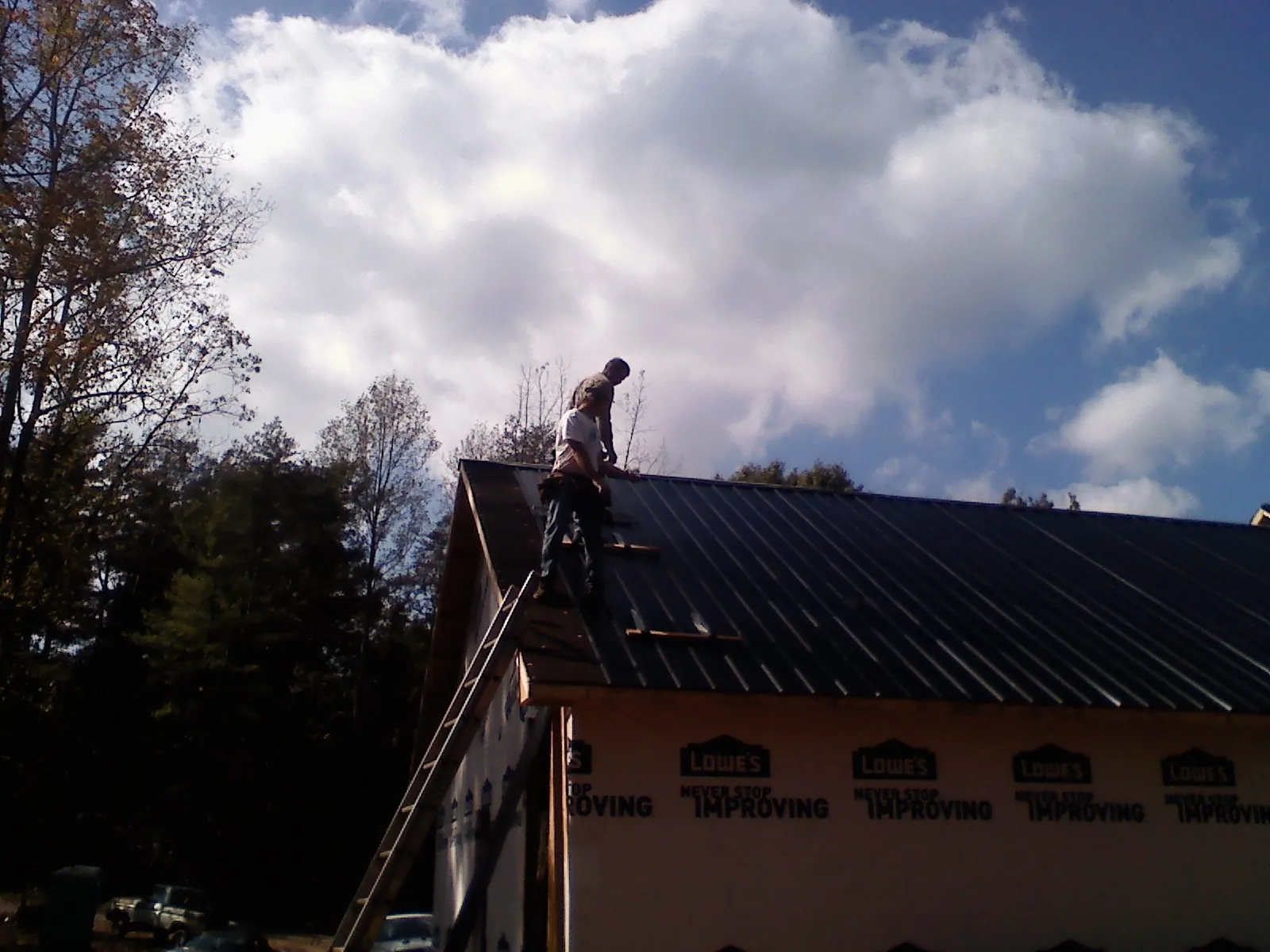 Roofer fastening dark metal panels high against a cloudy sky, from a Roof Inspection job in Sumter